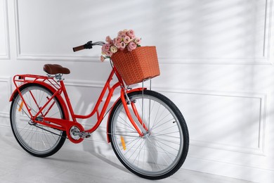 Photo of Bicycle with basket of beautiful flowers near white wall indoors. Space for text