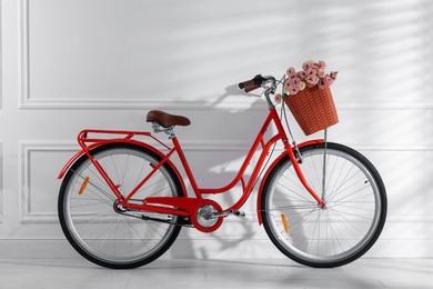 Photo of Bicycle with basket of beautiful flowers near white wall indoors