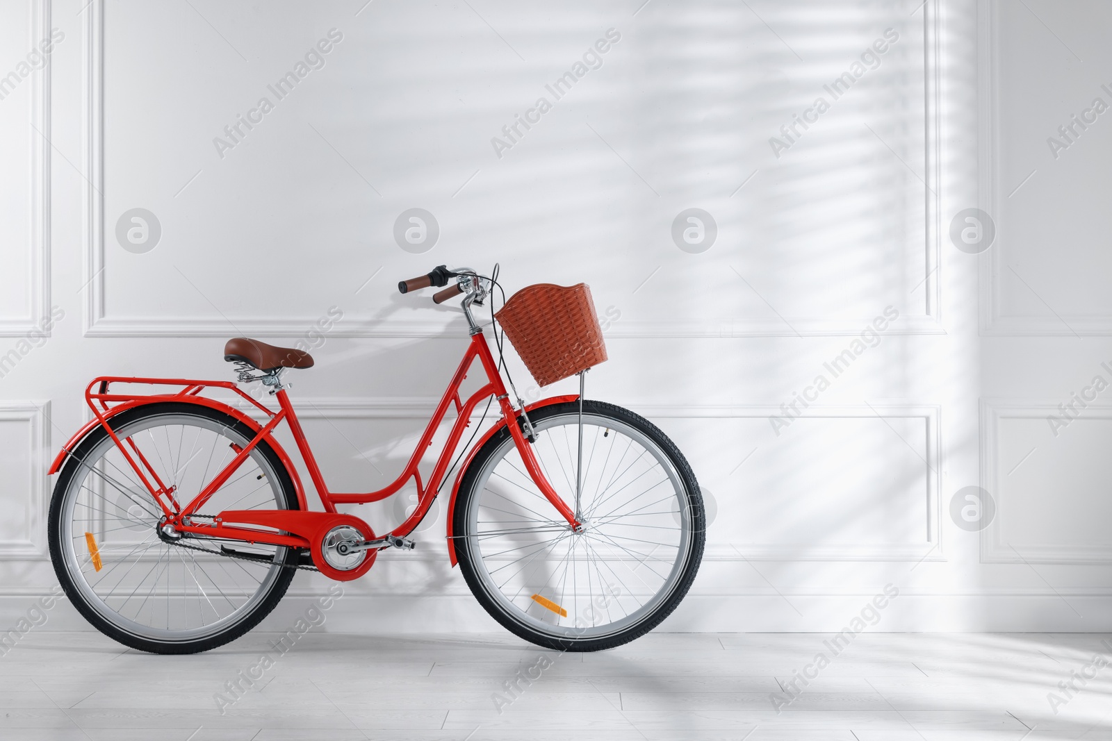 Red bicycle with basket near white wall indoors. Space for text Photo of Red bicycle with basket near white wall indoors. Space for text