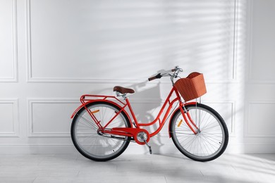 Photo of Red bicycle with basket near white wall indoors