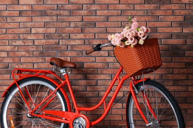 Photo of Bicycle with basket of beautiful flowers near brick wall indoors