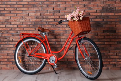 Photo of Bicycle with basket of beautiful flowers near brick wall indoors