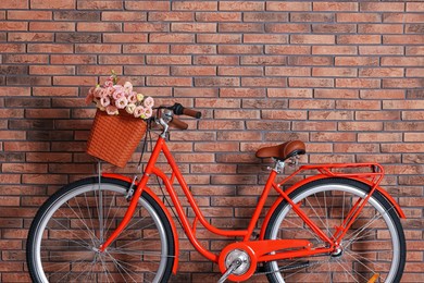 Photo of Bicycle with basket of beautiful flowers near brick wall indoors. Space for text