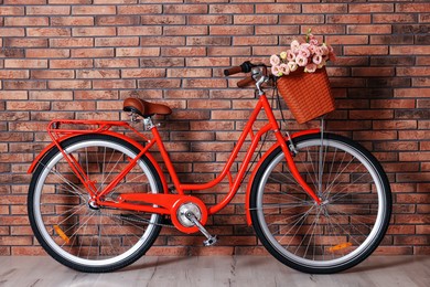 Photo of Bicycle with basket of beautiful flowers near brick wall indoors