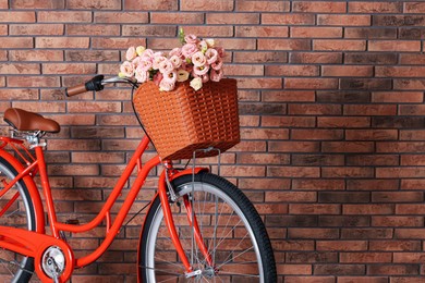 Photo of Bicycle with basket of beautiful flowers near brick wall indoors, closeup. Space for text