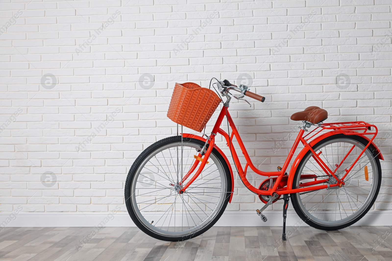 Red bicycle with basket near white brick wall indoors. Space for text Photo of Red bicycle with basket near white brick wall indoors. Space for text