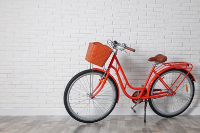 Photo of Red bicycle with basket near white brick wall indoors. Space for text