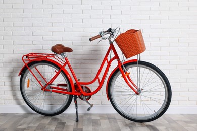 Photo of Red bicycle with basket near white brick wall indoors