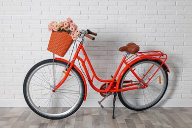 Photo of Bicycle with basket of beautiful flowers near white brick wall indoors