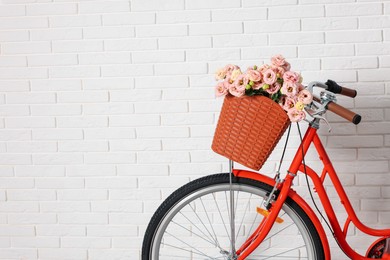 Photo of Bicycle with basket of beautiful flowers near white brick wall indoors, closeup. Space for text
