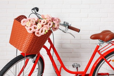 Photo of Bicycle with basket of beautiful flowers near white brick wall indoors, closeup