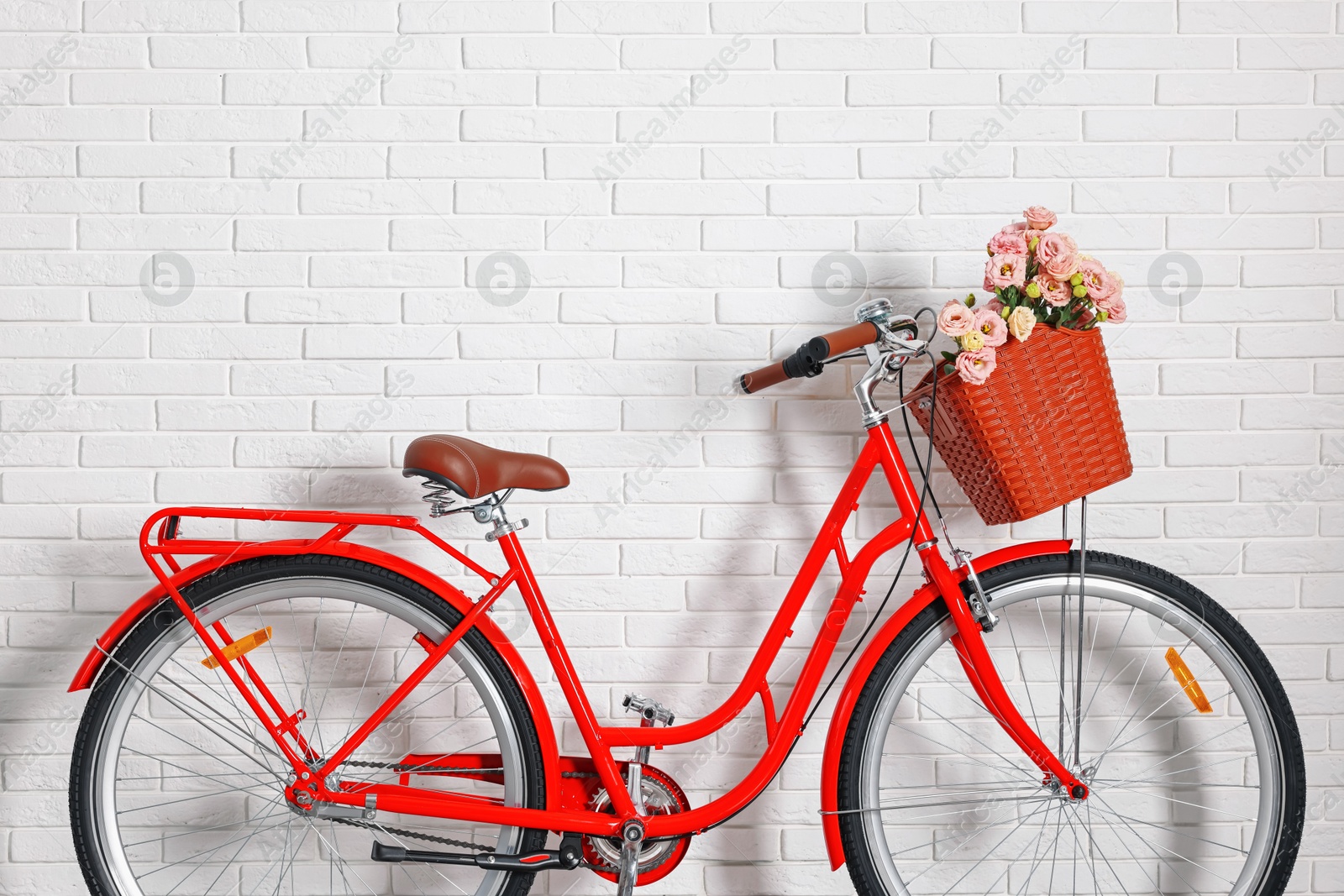 Bicycle with basket of beautiful flowers near white brick wall indoors Photo of Bicycle with basket of beautiful flowers near white brick wall indoors