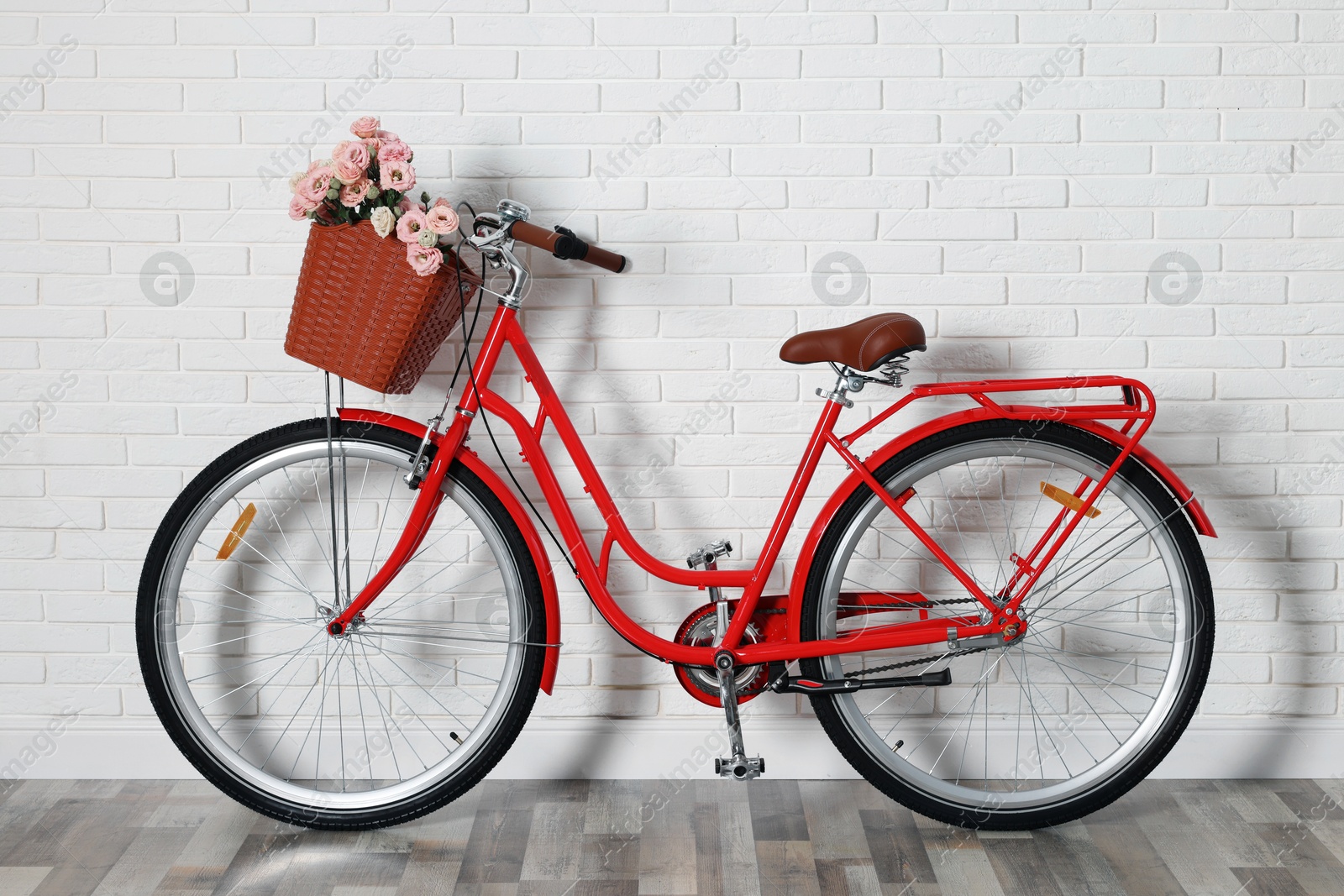 Bicycle with basket of beautiful flowers near white brick wall indoors Photo of Bicycle with basket of beautiful flowers near white brick wall indoors
