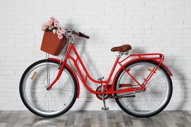 Photo of Bicycle with basket of beautiful flowers near white brick wall indoors