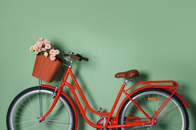 Photo of Bicycle with basket of beautiful flowers near light green wall indoors. Space for text
