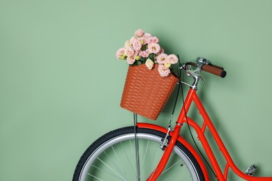 Photo of Bicycle with basket of beautiful flowers near light green wall indoors, closeup. Space for text