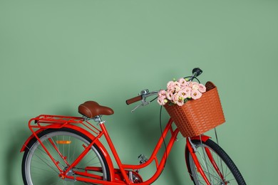 Photo of Bicycle with basket of beautiful flowers near light green wall indoors. Space for text