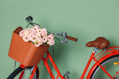 Photo of Bicycle with basket of beautiful flowers near light green wall indoors, closeup