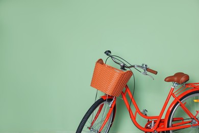 Photo of Red bicycle with basket near light green wall indoors. Space for text