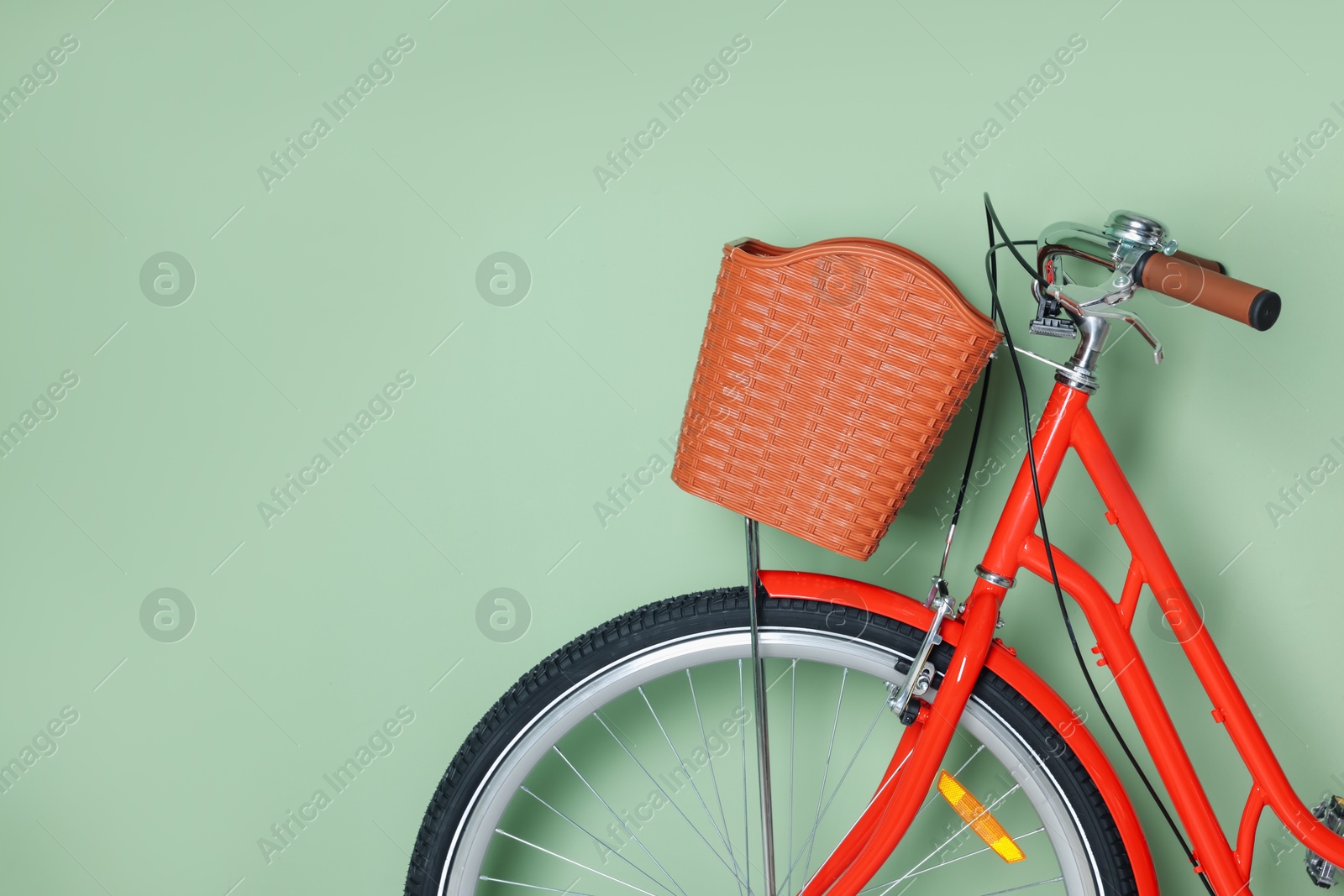 Photo of Red bicycle with basket near light green wall indoors, closeup. Space for text