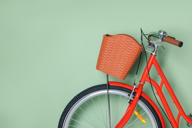 Photo of Red bicycle with basket near light green wall indoors, closeup. Space for text
