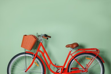 Photo of Red bicycle with basket near light green wall indoors. Space for text