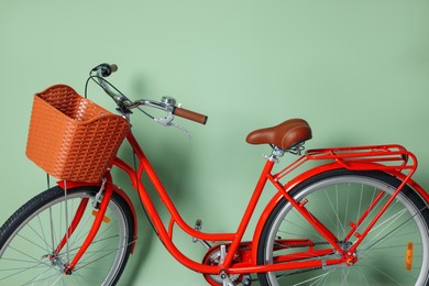 Photo of Red bicycle with basket near light green wall indoors, closeup