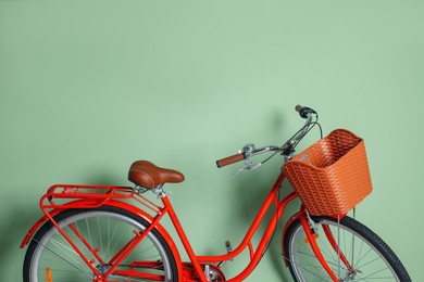 Photo of Red bicycle with basket near light green wall indoors. Space for text