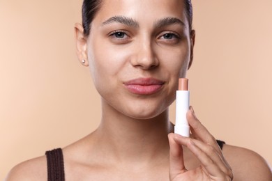 Photo of Young woman with lip balm on beige background