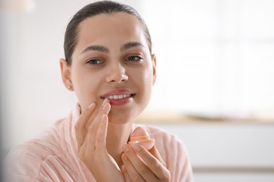 Photo of Young woman with lip balm at home, space for text