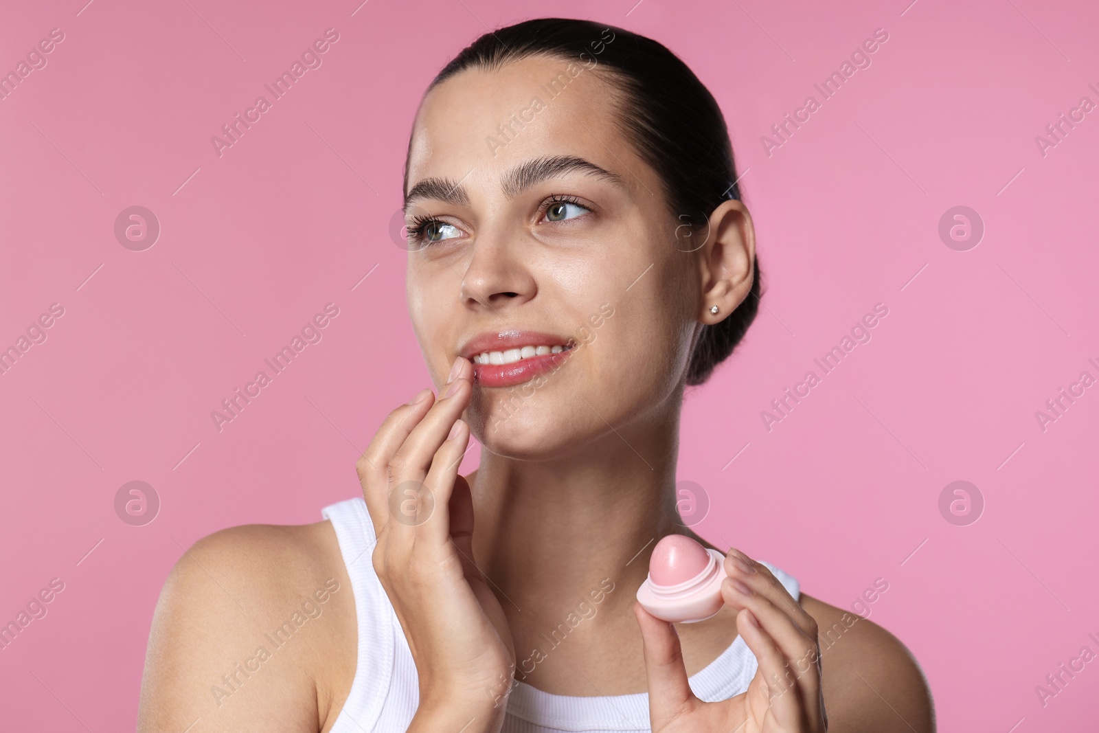 Young woman with lip balm on pink background Photo of Young woman with lip balm on pink background