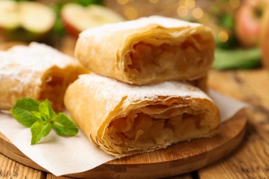 Photo of Pieces of tasty apple strudel with powdered sugar and mint on wooden table, closeup