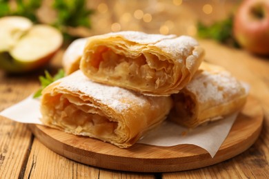 Photo of Pieces of tasty apple strudel with powdered sugar on wooden table, closeup