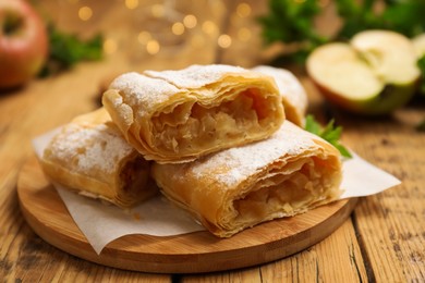 Photo of Pieces of tasty apple strudel with powdered sugar on wooden table, closeup