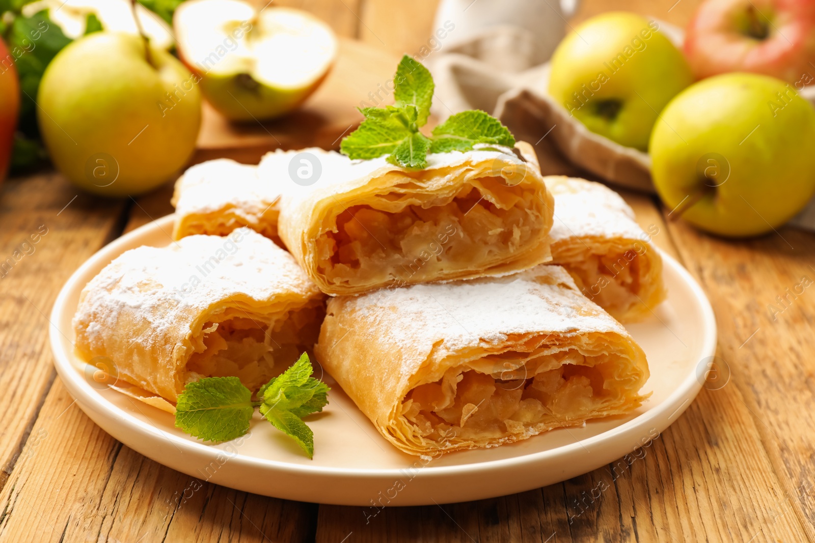 Pieces of tasty apple strudel with powdered sugar, mint and fruits on wooden table, closeup Photo of Pieces of tasty apple strudel with powdered sugar, mint and fruits on wooden table, closeup