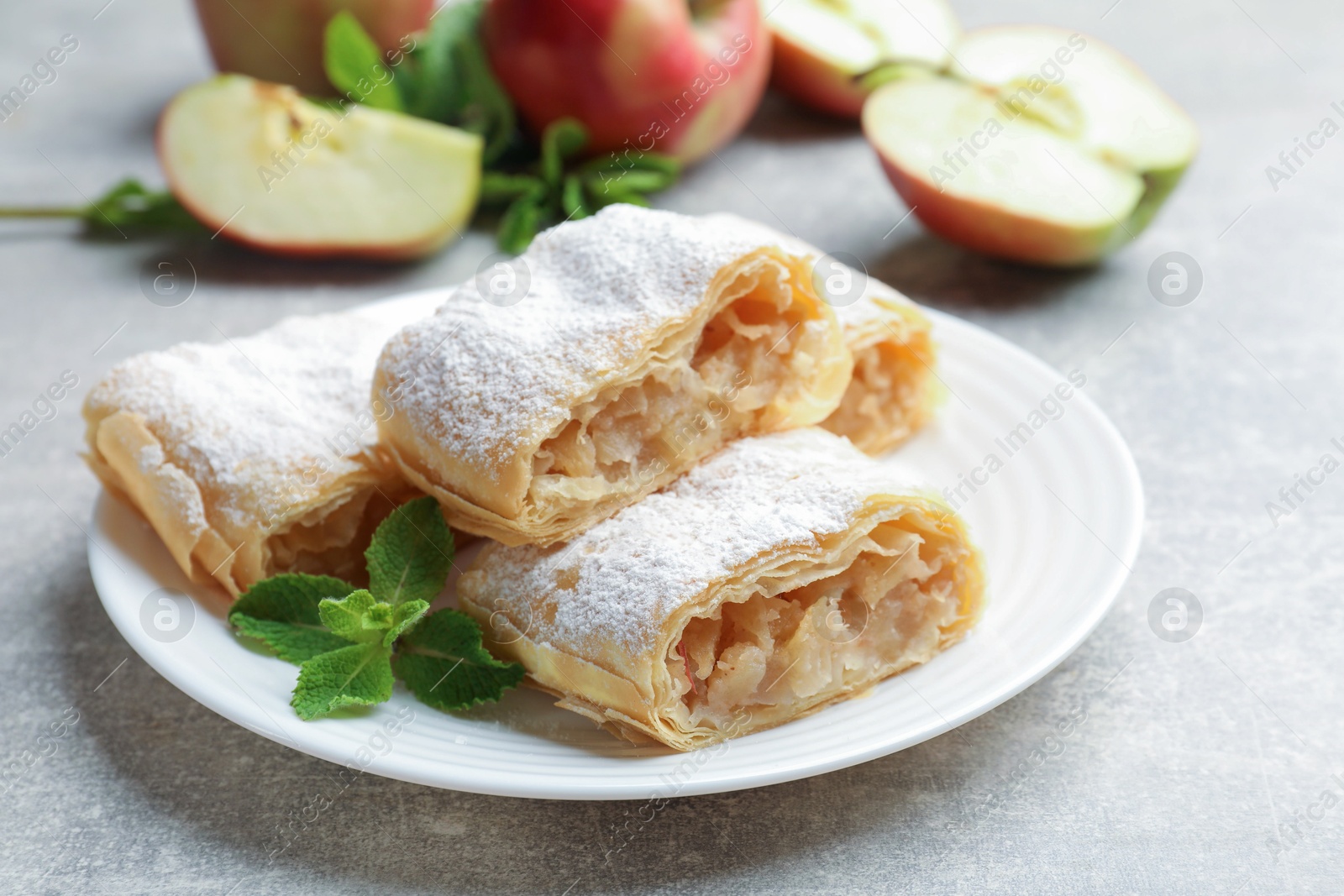 Pieces of tasty apple strudel with powdered sugar and mint on light grey table, closeup Photo of Pieces of tasty apple strudel with powdered sugar and mint on light grey table, closeup