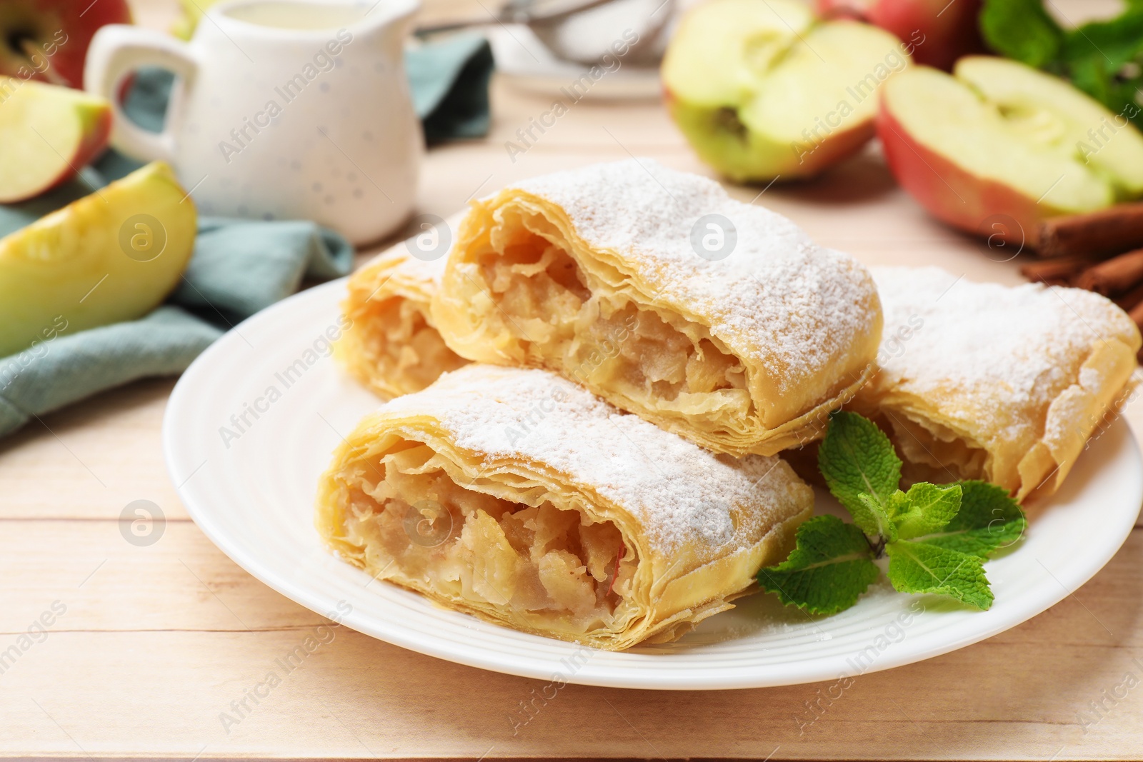 Pieces of tasty apple strudel with powdered sugar and mint on light wooden table, closeup Photo of Pieces of tasty apple strudel with powdered sugar and mint on light wooden table, closeup