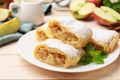 Photo of Pieces of tasty apple strudel with powdered sugar and mint on light wooden table, closeup