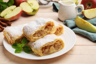 Photo of Pieces of tasty apple strudel with powdered sugar and mint on light wooden table, closeup