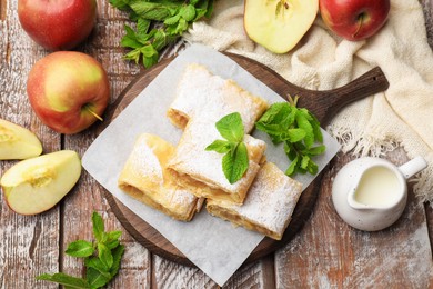 Photo of Pieces of tasty apple strudel with powdered sugar, mint and fruits on wooden table, flat lay