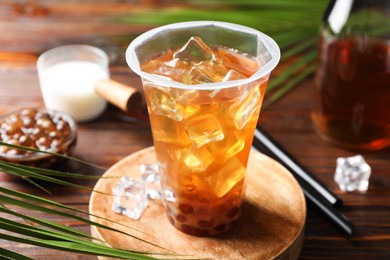 Photo of Tasty iced bubble tea and ingredients on wooden table, closeup