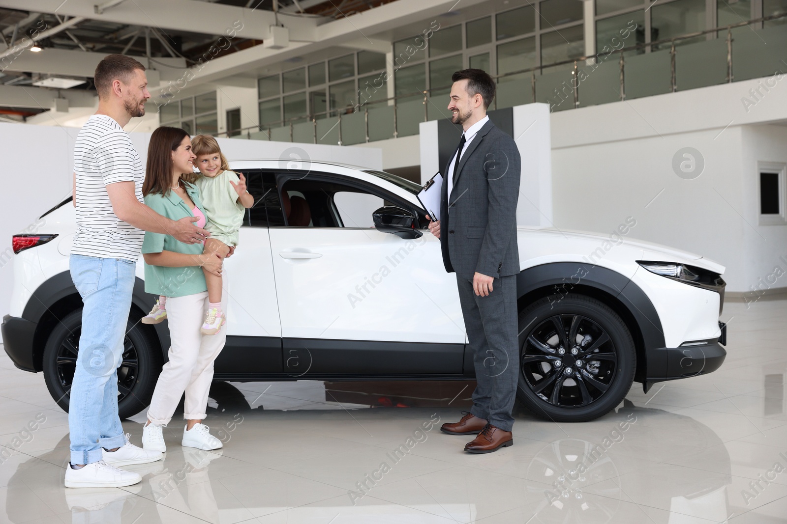 Smiling salesman with clipboard showing new car to family in salon Photo of Smiling salesman with clipboard showing new car to family in salon