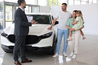 Photo of Salesman with clipboard showing new car to happy family in salon