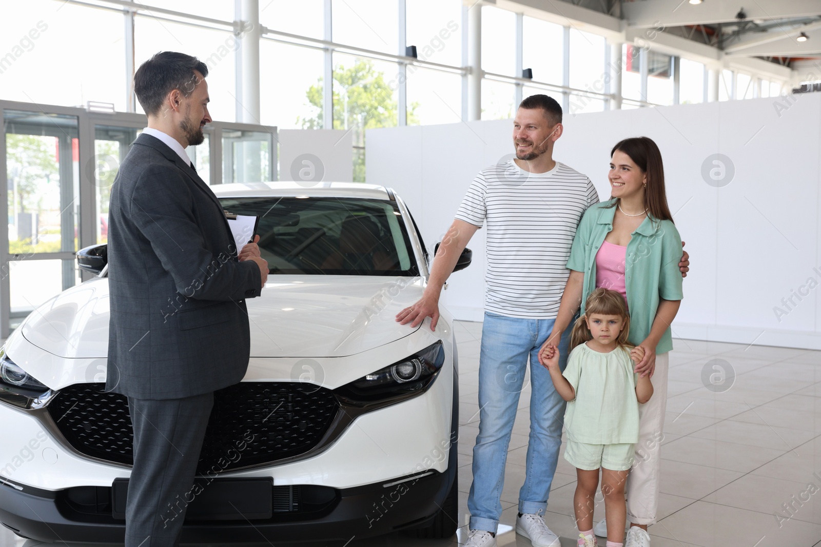 Photo of Salesman with clipboard showing new car to happy family in salon