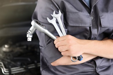 Photo of Auto parts. Professional mechanic with different wrenches near open hood of car indoors, closeup. Space for text