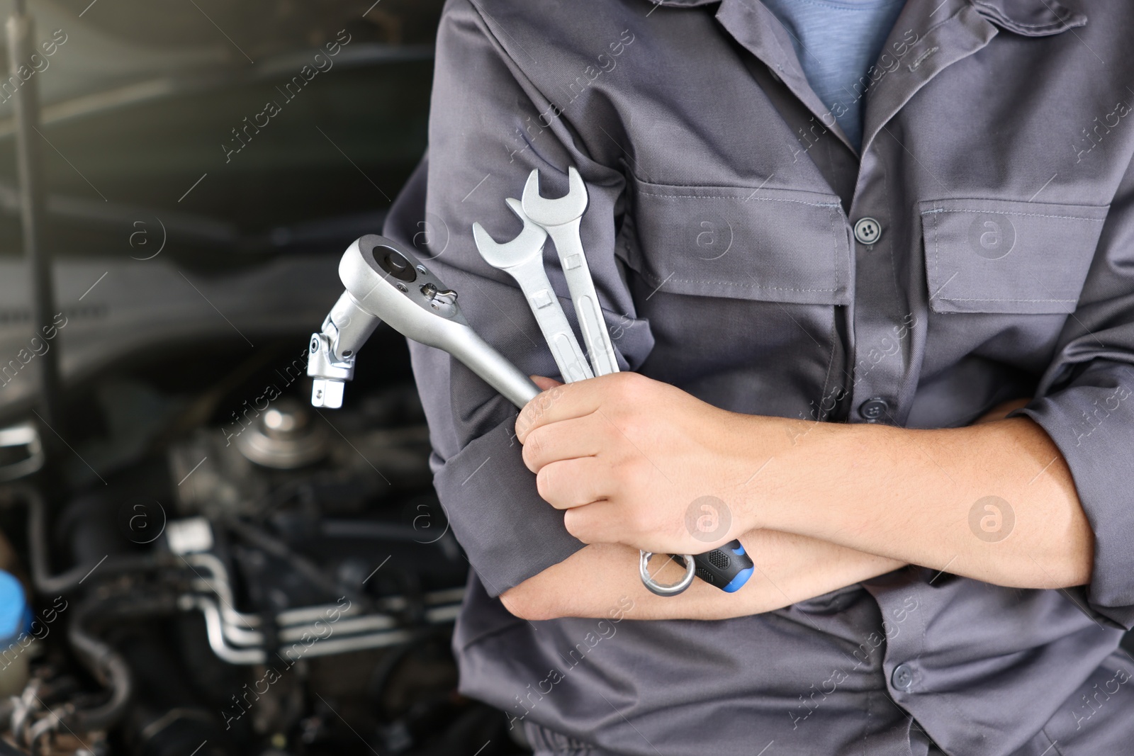Auto parts. Professional mechanic with different wrenches near open hood of car indoors, closeup. Space for text Photo of Auto parts. Professional mechanic with different wrenches near open hood of car indoors, closeup. Space for text