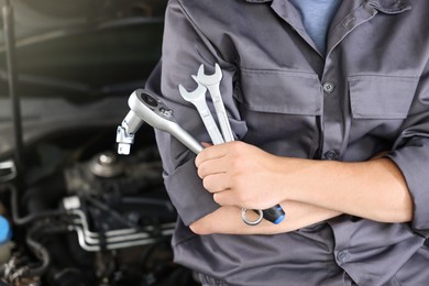 Photo of Auto parts. Professional mechanic with different wrenches near open hood of car indoors, closeup. Space for text