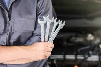Photo of Auto parts. Professional mechanic with different wrenches near open hood of car indoors, closeup. Space for text