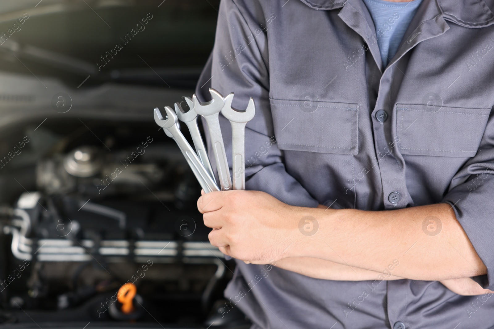 Auto parts. Professional mechanic with different wrenches near open hood of car indoors, closeup. Space for text Photo of Auto parts. Professional mechanic with different wrenches near open hood of car indoors, closeup. Space for text