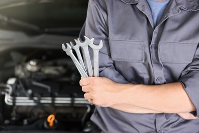 Photo of Auto parts. Professional mechanic with different wrenches near open hood of car indoors, closeup. Space for text